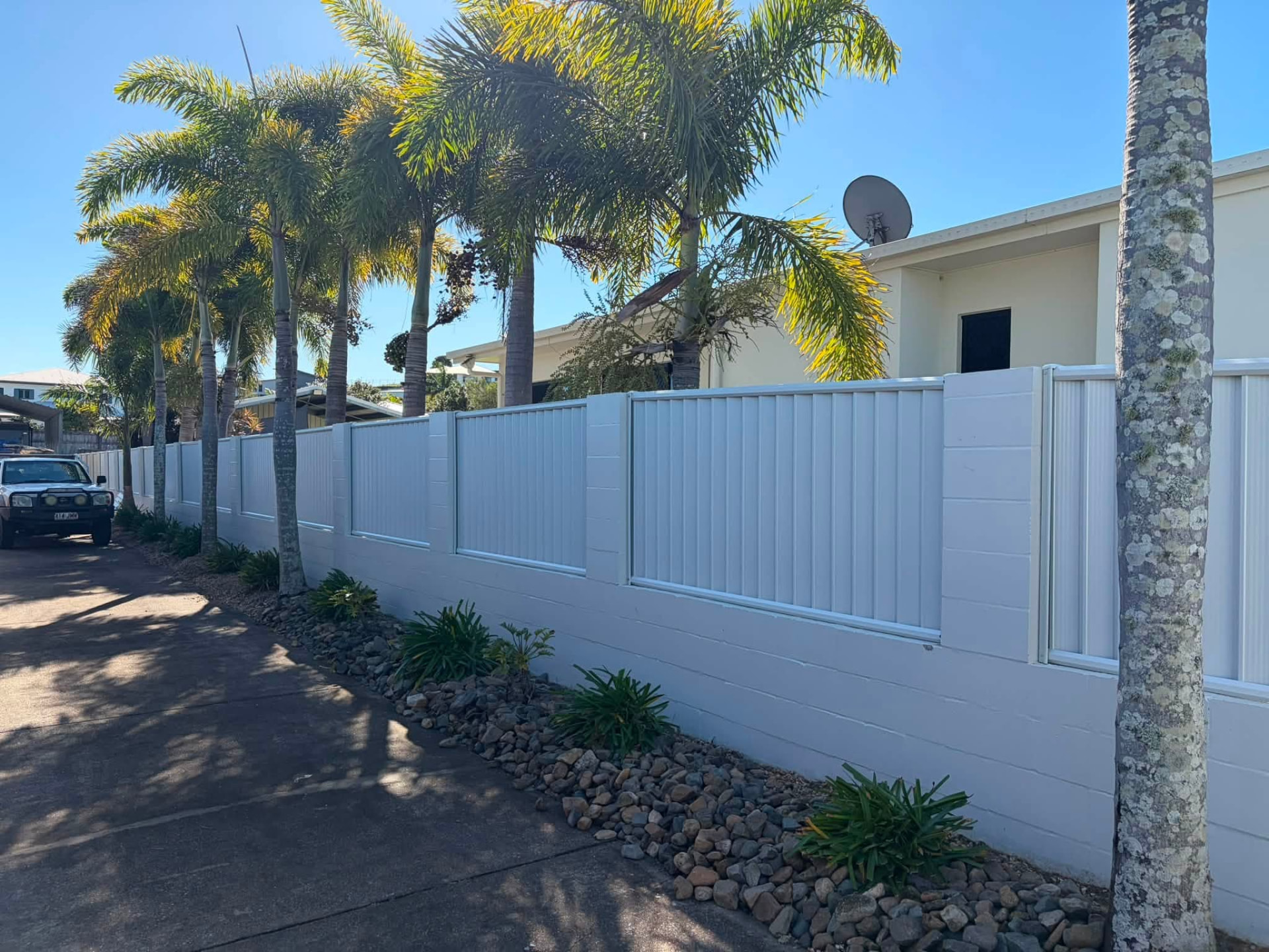 New light-coloured panel fence with a retaining base along a palm-lined driveway